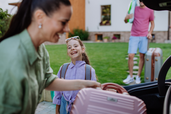 Happy family preparing for a holiday, putting suitcases in a car trunk, while their electric car charging.