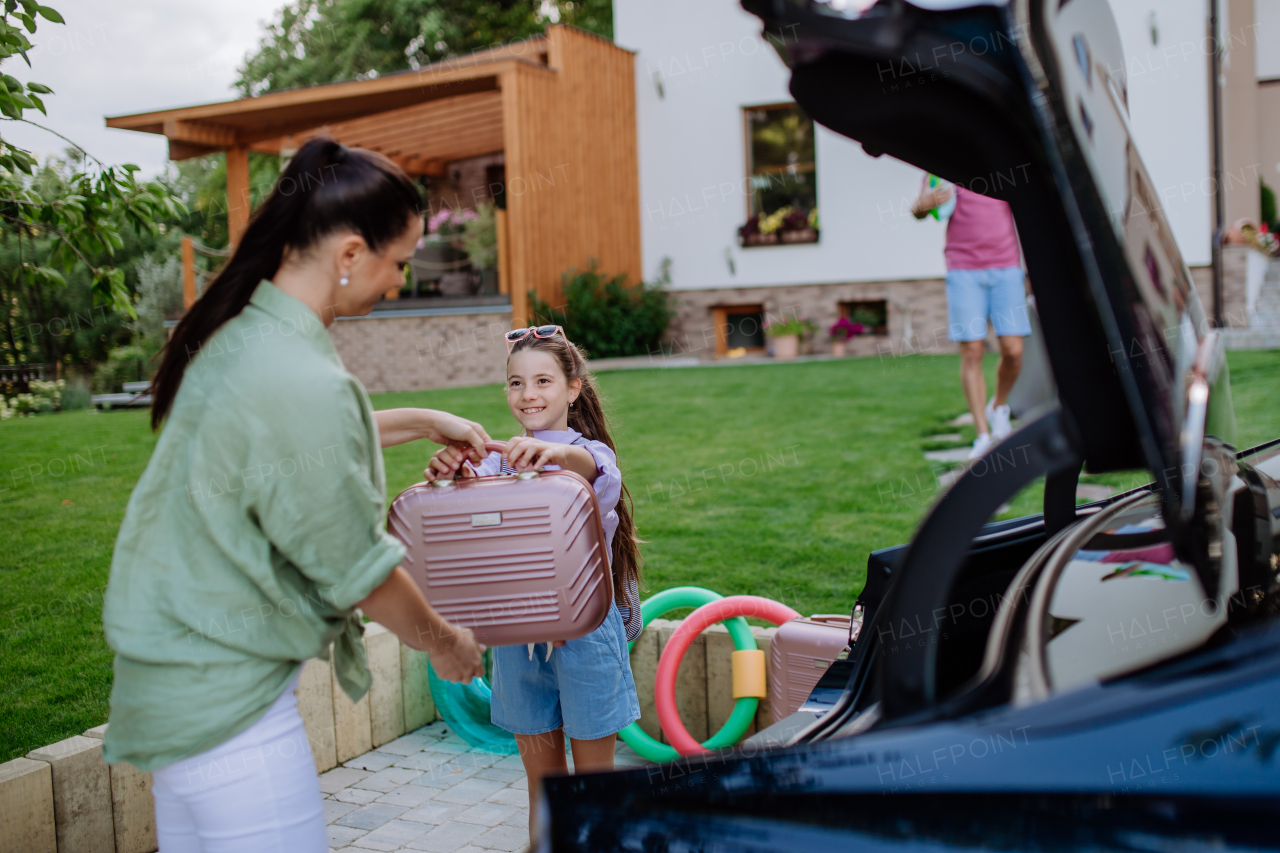 Happy family preparing for a holiday, putting suitcases in a car trunk, while their electric car charging.