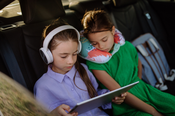 LIttle girl looking in digital tablet and listening music, her sister fall asleep during family trip in car.