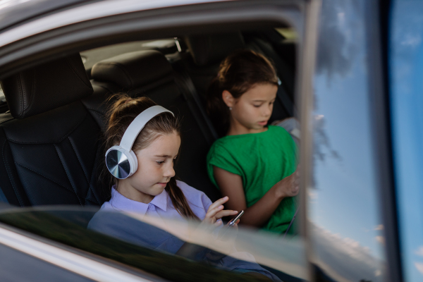 Little sisters sitting in a car, listening to music and waiting for a car trip.