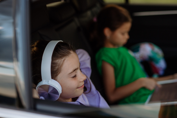 Little sisters sitting in a car, listening to music and waiting for a car trip.