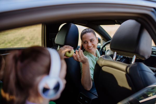 Mother giving apple to her daughter in a car.