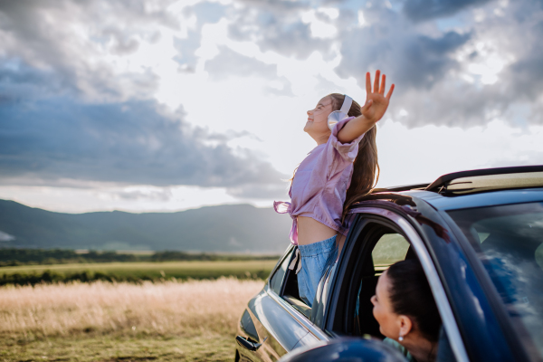 Little girl with a headphones standing and leaning out of the car window during the ride.