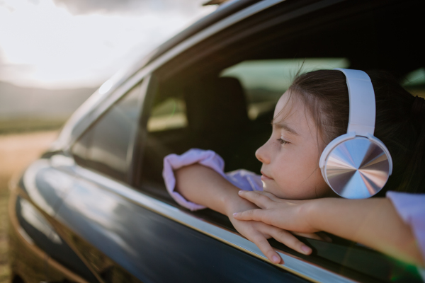 Little girl with a headphones looking out of the car window during the ride.