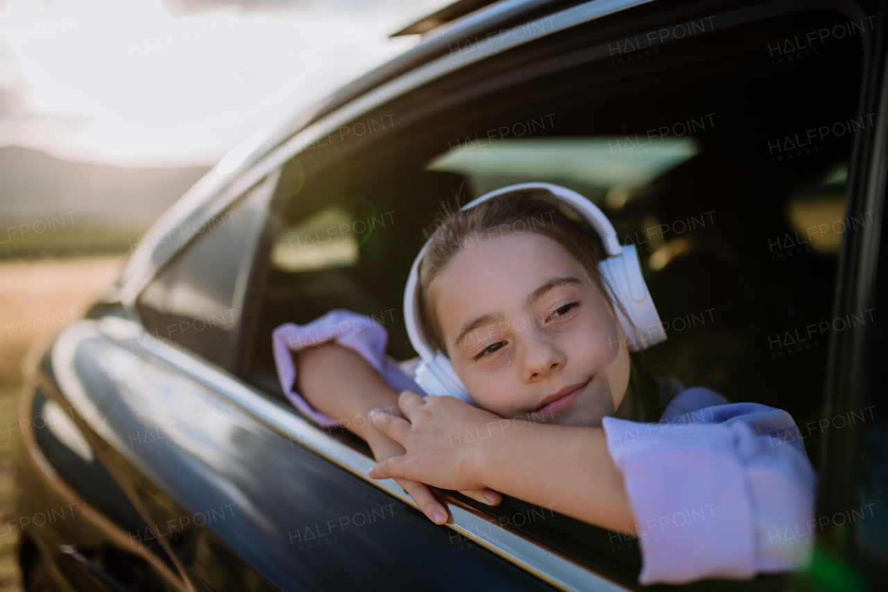 Little girl with a headphones looking out of the car window during the ride.