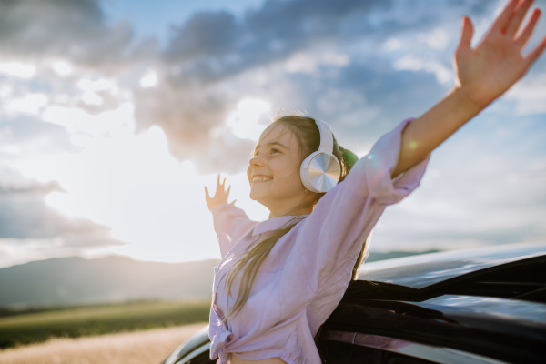 Little girl with a headphones standing and leaning out of the car window during the ride.