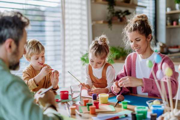 Happy family with little kids decorating easter eggs in their home.