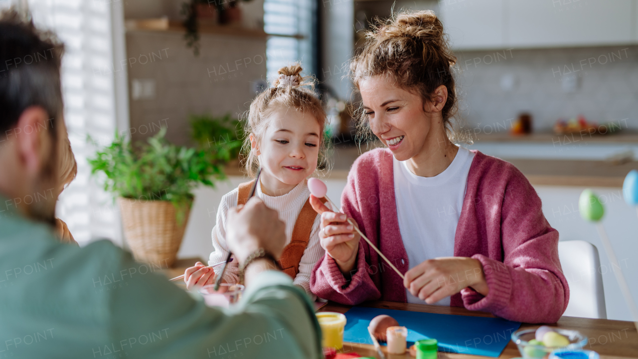 Happy family with little child decorating easter eggs in their home.