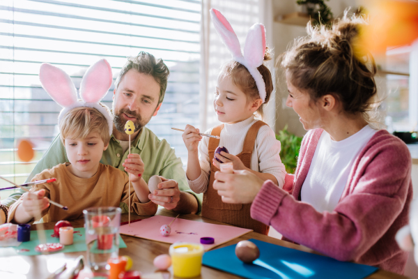 Happy family with little kids decorating easter eggs in their home.