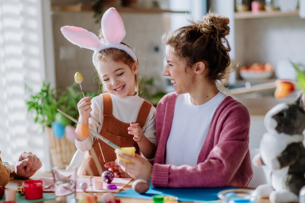 Happy mother with her little daughter decorating easter eggs in their home.