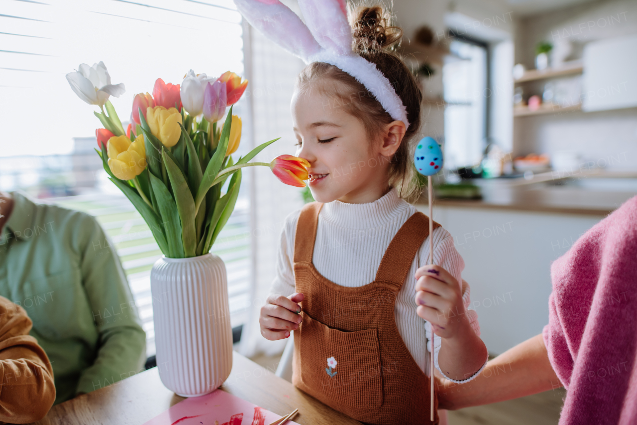 Little girl smelling bouquet of tulip flowers during decorating the easter eggs with her family.