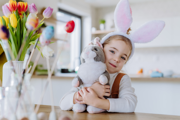 Portrait of little girl with bunny ears, bunny soft toy, celebrating easter and spring.