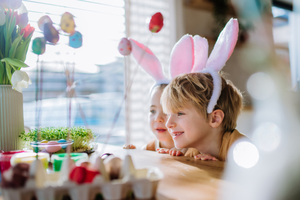 Happy siblings looking at growing plant after decorating easter eggs.