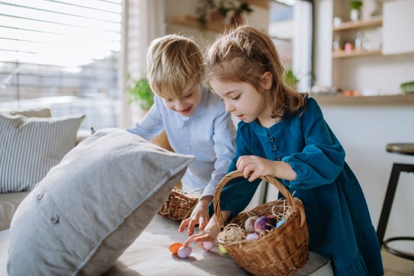 Happy little girl with her brother looking for easter eggs in their home.