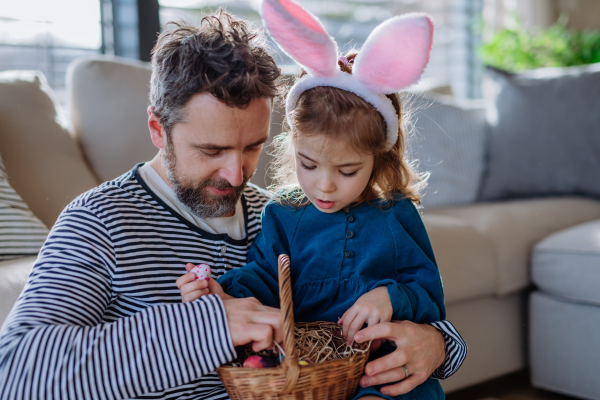 Little girl with bunny ears holding basket and showing father easter eggs which she found.