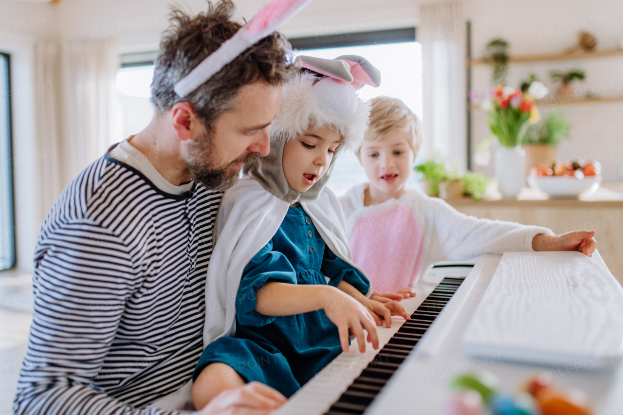 Happy kids in Easter costumes playing on the piano, with their father.