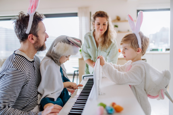 Happy family with small children in easter costumes playing on the piano.