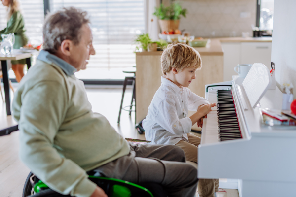 Little boy playing on the piano with his grandfather on the wheelchair.