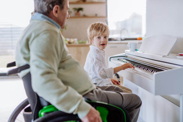 Little boy playing on the piano with his grandfather on the wheelchair.