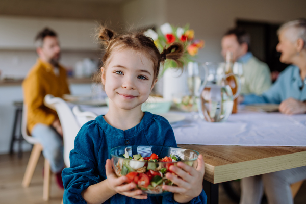 Little girl holding bowl with salad, preparations for a family dinner.