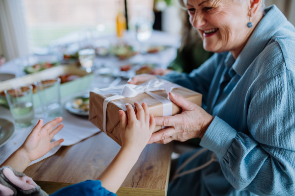 Grandmother giving gift to her granddaughter during an Easter dinner, close-up.