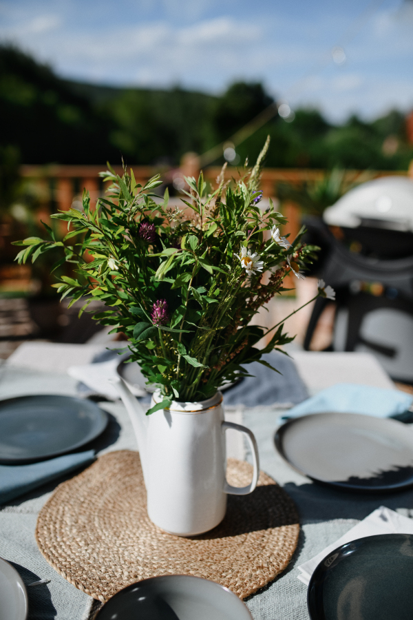 A dining table with bouquet set for dinner on the terrace with grill in summer, garden party. concept.