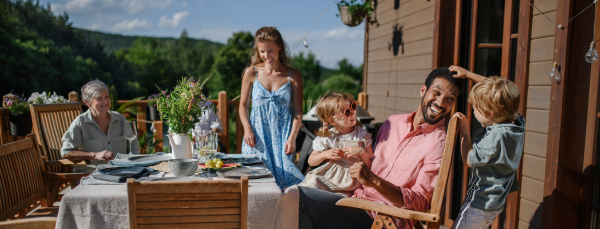 Three generations family having fun at barbecue party dinner on patio, people sitting at table on patio with grill.