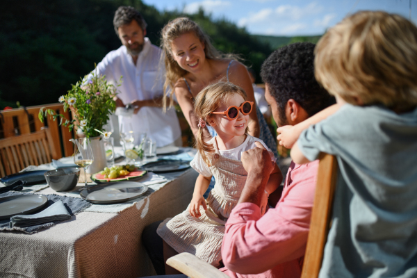 A family with kids having fun at barbecue party dinner on patio, people sitting at table on patio and talking