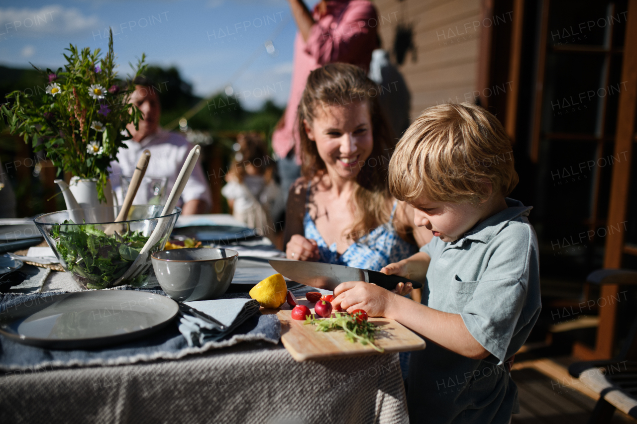 Happy family preparing for outdoor grill party, little boy cutting the vegetable.