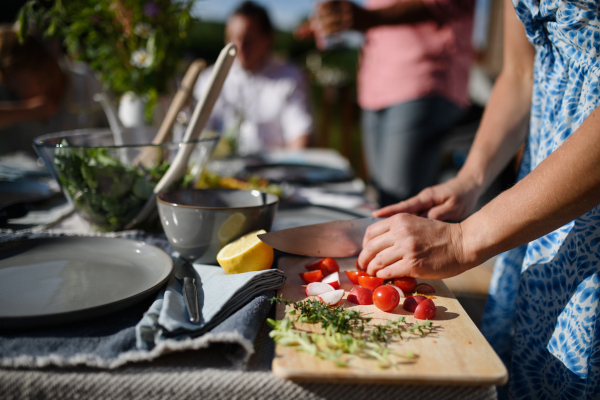 An unrecognizable woman cutting vegetables on wooden board during weekend barbecue in yard, outdoor, prepare for grilling,