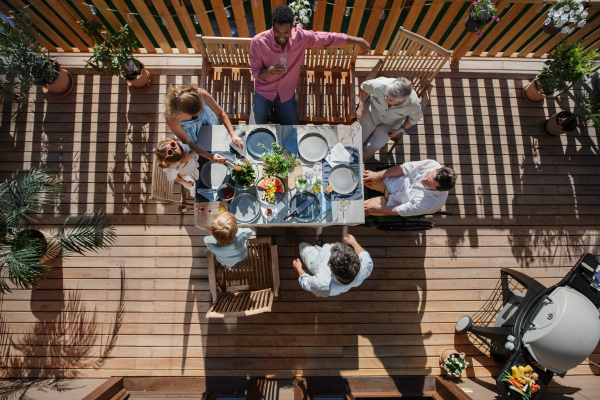 A top view of 3 generations family eating at barbecue party dinner on patio, people sitting on patio with grill.