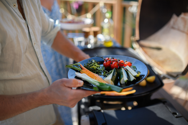 An unrecognizable man grilling vegetable on grill during family summer garden party.