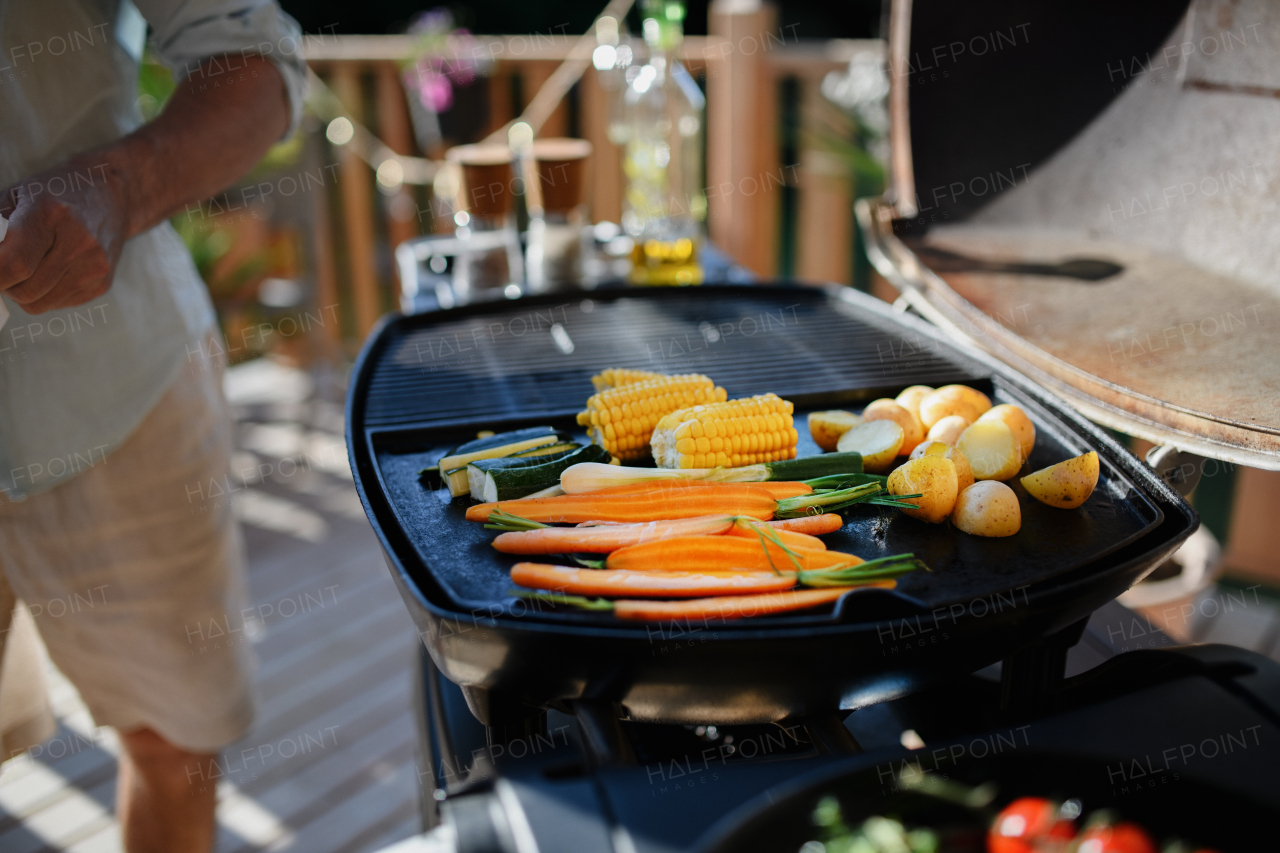 An unrecognizable man grilling vegetable on grill during family summer garden party.