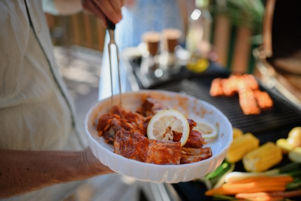 An unrecognizable man preparing meat and vegetables for grilling during family summer garden party, close-up