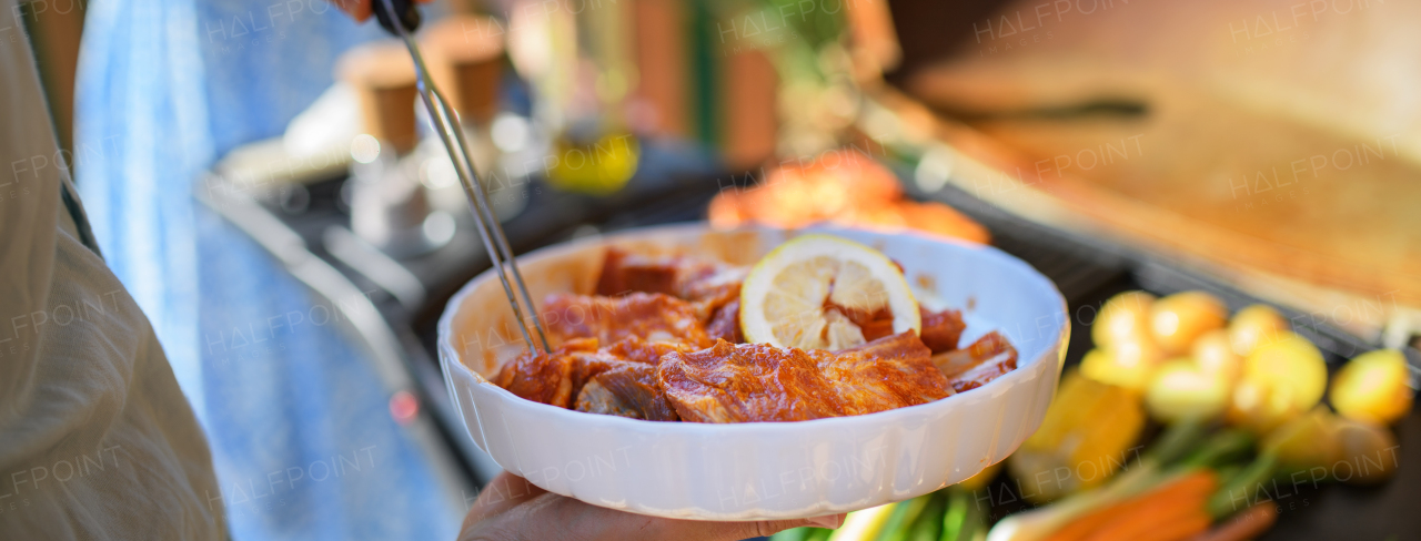 An unrecognizable man preparing meat and vegetables for grilling during family summer garden party, close-up