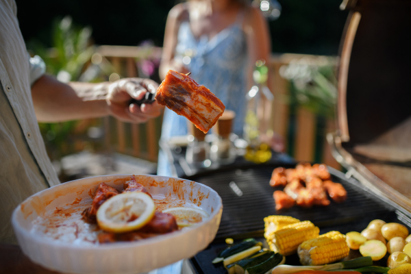 An unrecognizable man preparing meat and vegetables for grilling during family summer garden party, close-up