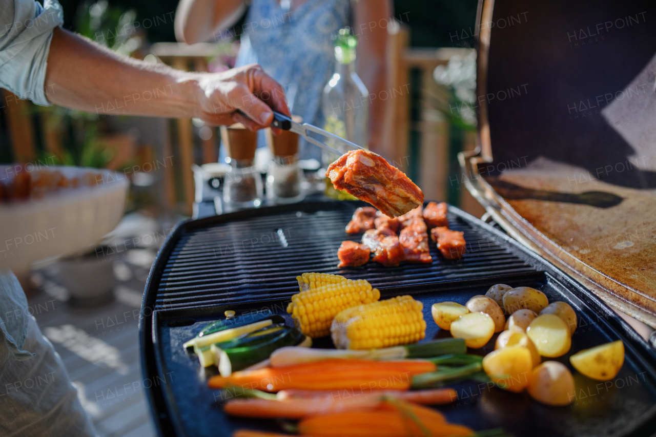 An unrecognizable man grilling ribs and vegetable on grill during family summer garden party