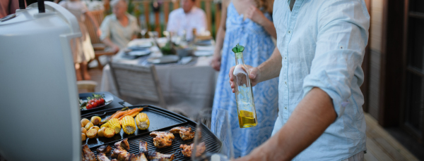 An unrecognizable man grilling ribs and vegetable on grill during family summer garden party