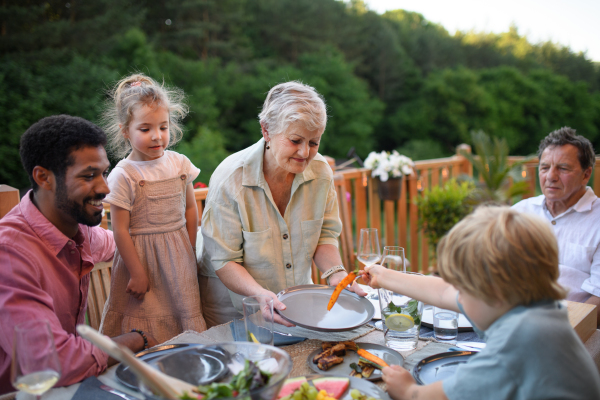 Multigenerational family eating dinner at outdoor barbecue party.