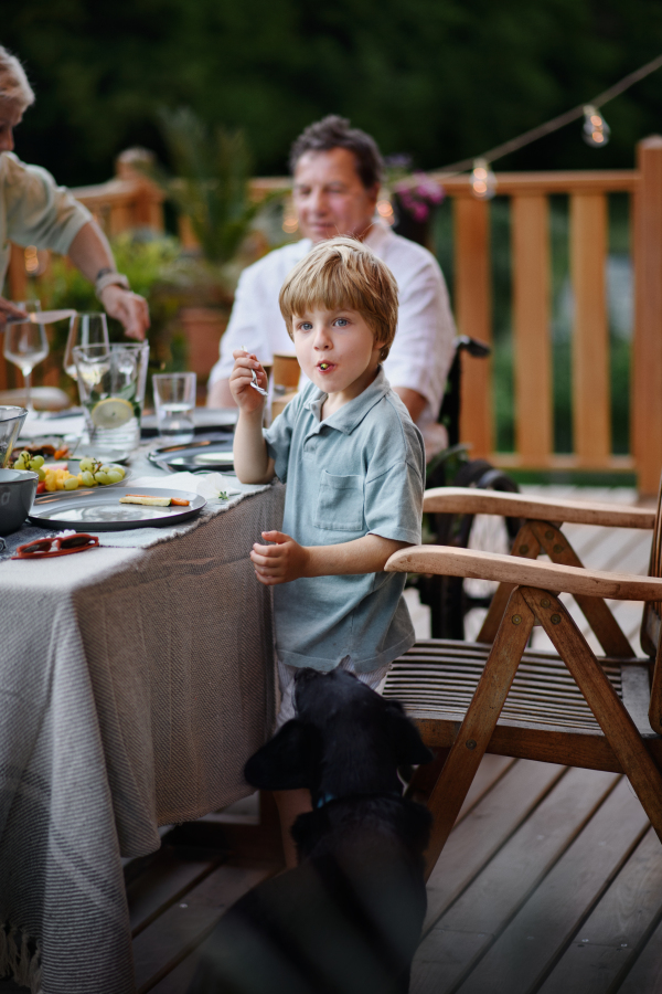 A family eating at barbecue party dinner on patio, little boy eating grilles vegetables and enjoying it.