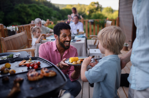 A father grilling meat and vegetable on grill during family summer garden party.