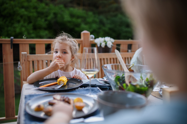 A family eating at barbecue party dinner on patio, little girl eating roasted corn and enjoying it.