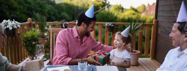 A multi generation family celebratiing birthday and have garden party outside in the backyard on patio.