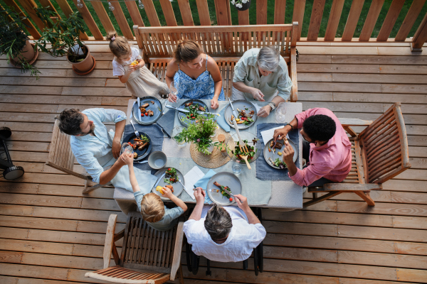 A top view of 3 generations family eating at barbecue party dinner on patio, people sitting on patio with grill.