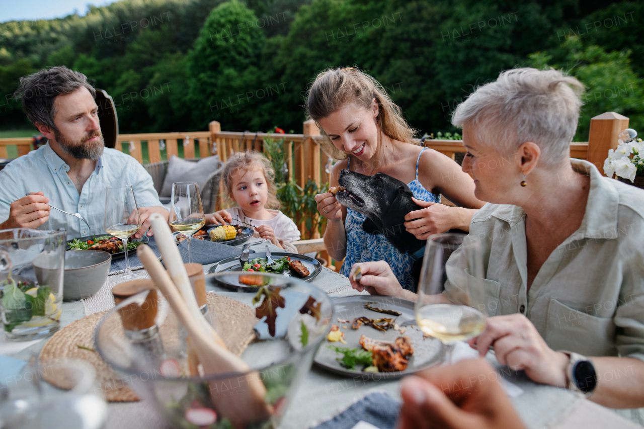 Multigenerational family eating dinner at outdoor barbecue party.