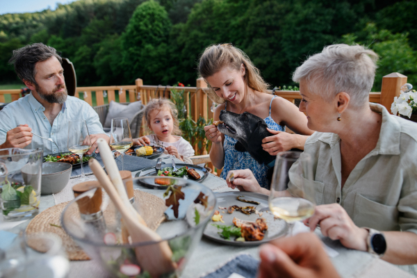 Multigenerational family eating dinner at outdoor barbecue party.