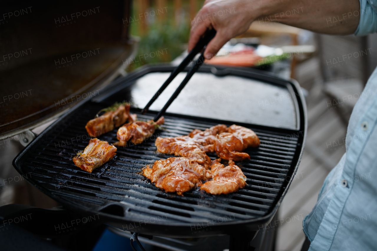 An unrecognizable man grilling meat, ribs and wings, on grill during family summer garden party, close-up