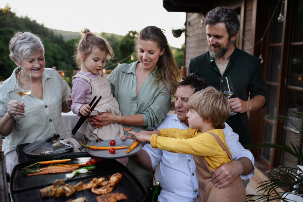 A multi generation family grilling outside on patio in summer during garden party