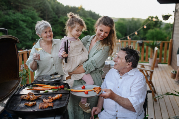 A multi generation family grilling outside on patio in summer during garden party