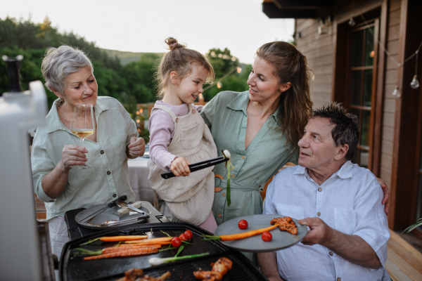 A multi generation family grilling outside on patio in summer during garden party